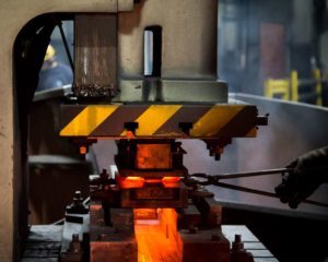 A preheated metal billet (preform) is being placed into a mechanical forging press