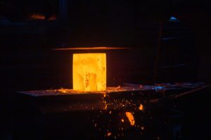 close-up picture of hot steel manual forging process with big mechanical hammer machine