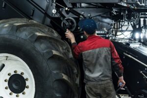 An industrial worker in a black and grey jumpsuit assembles a combine harvester