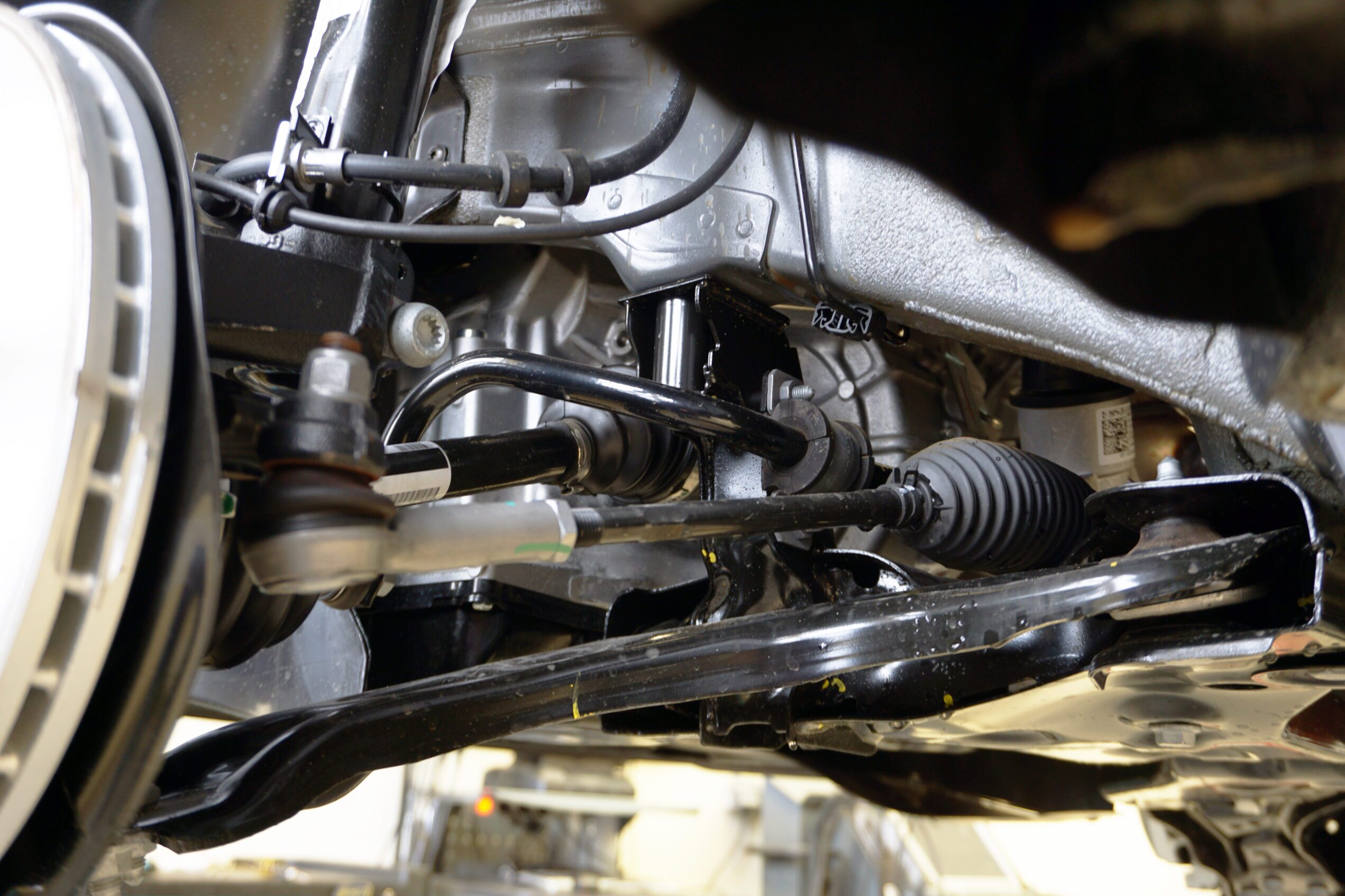 A close of up a front suspension of a car, including the suspension arm, steering rod and tip, drive shaft, anthers, and stabilizer